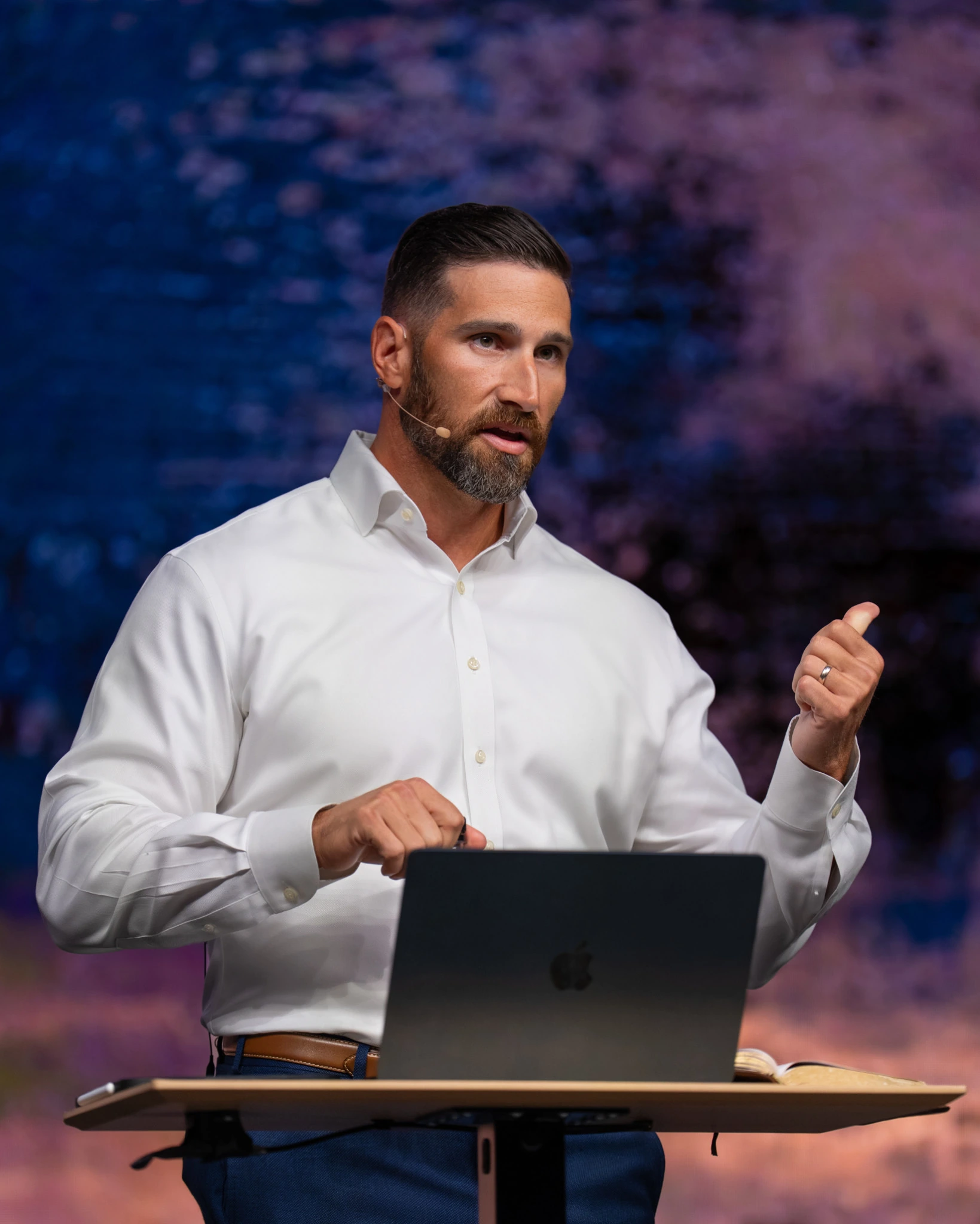 The speaker discussing passages from the Bible behind a lectern with a laptop and open Bible at Ascend Church.