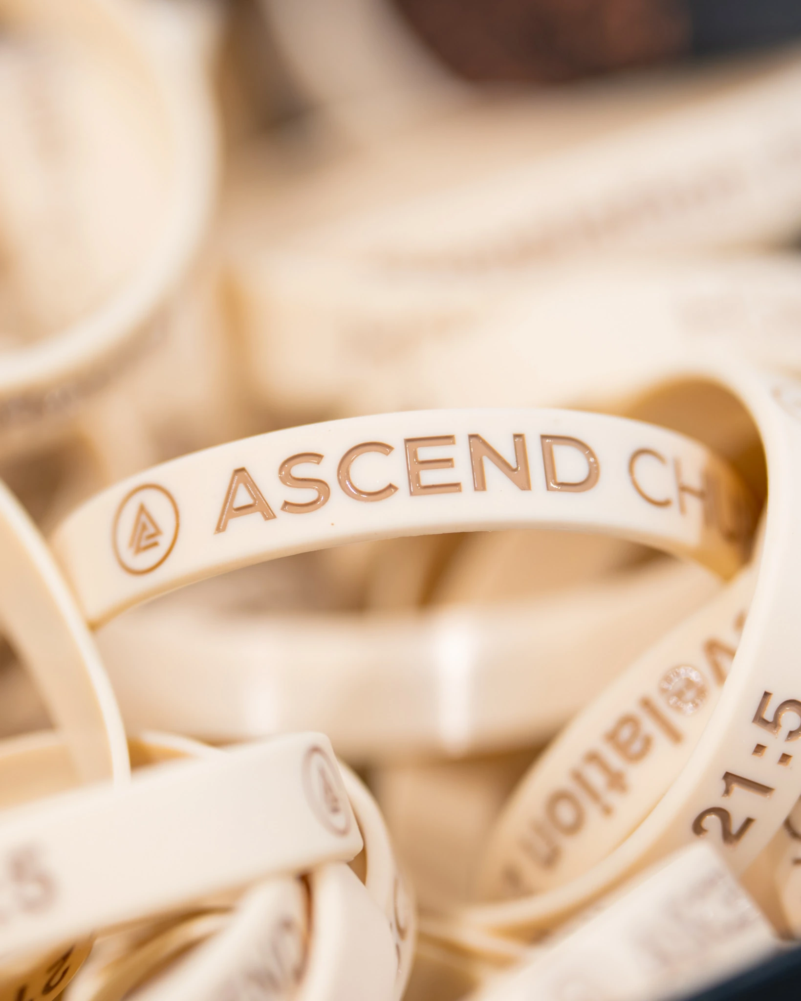 Close-up of cream wristbands with gold Ascend Church lettering and logo in the merchandise area.